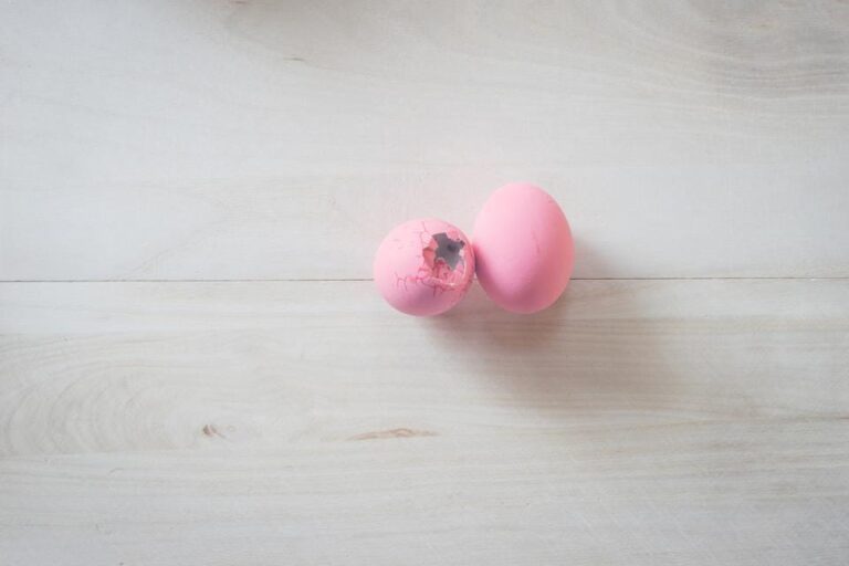 Two egg shells painted pink, the one on the left is cracked and broken
