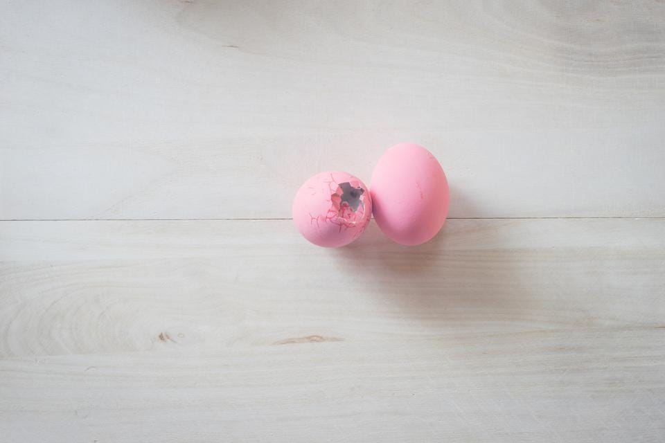 Two egg shells painted pink, the one on the left is cracked and broken